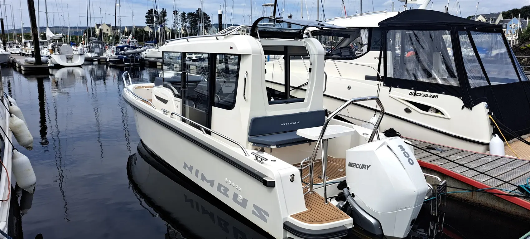 Nimbus boat docked at a marina, featuring a Mercury 300 engine and a spacious cabin with seating and a table.